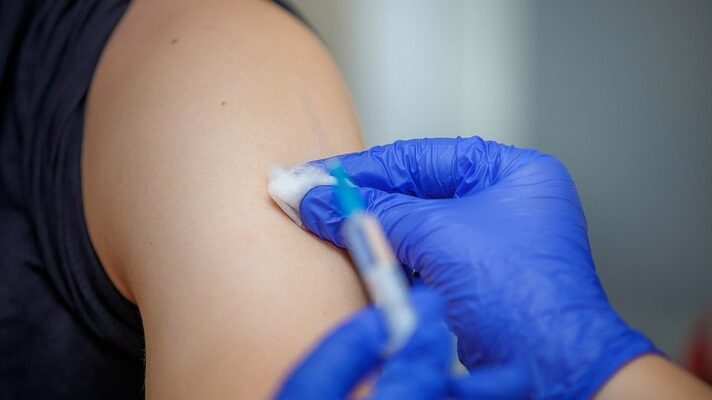 A healthcare professional wearing sterile gloves administers an injection into a patient's arm